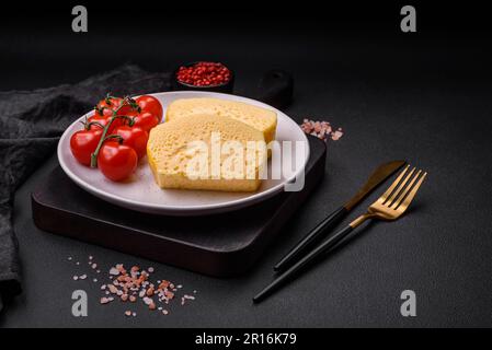 Köstliches Omelett mit Milch, Gewürzen und Kräutern, die auf einer Keramikplatte auf dunklem Betonhintergrund in große Stücke geschnitten wurden Stockfoto