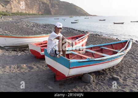 Mann sitzt auf einem traditionellen hölzernen Fischerboot an einem Strand in einem kleinen Fischerdorf von tarrafal de monte trigo auf der insel santo antao, cabo verde Stockfoto