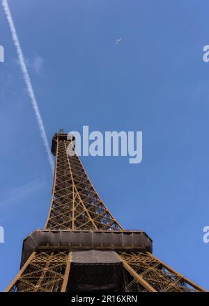 Eiffelturm von unten vor dem klaren blauen Himmel mit Kontrasten und einem entfernten Flugzeug Stockfoto