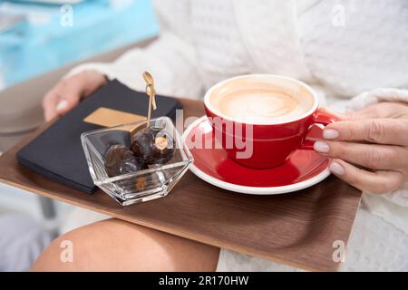 Frau im Bademantel sitzt mit einer Tasse Kaffee und Obst Stockfoto
