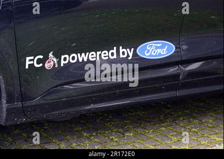 Köln, Deutschland. 11. Mai 2023. Der Schriftzug „FC powered by Ford“ und ein blaues Ford-Logo auf einem Auto. Ford ist der exklusive Sponsor des 1. FC Köln. Spieler, Trainer und das Präsidium können aus der gesamten Fahrzeugflotte wählen. Kredit: Horst Galuschka/dpa/Alamy Live News Stockfoto