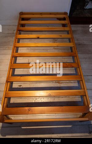 Ein Einzelbett aus Holz in einem kleinen Zimmer mit einer roten Tür und weiß gewaschenen Bodenbrettern Stockfoto