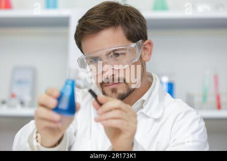 Wissenschaftler pipettieren blaue Flüssigkeit in Reagenzgläser Stockfoto