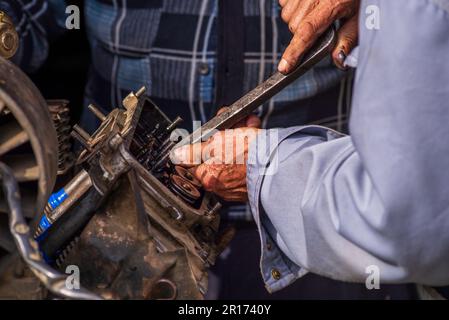 Zwei alte Männer, Automechaniker, die an rostigem Motor arbeiten, in einer Werkstatt. Reparaturservice Nahaufnahme zerknitterte schmutzige Hände blaue Kleidung Gear Truck DISAs Stockfoto