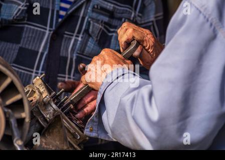 Zwei alte Männer, Automechaniker, die an rostigem Motor arbeiten, in einer Werkstatt. Reparaturservice Nahaufnahme zerknitterte schmutzige Hände blaue Kleidung Gear Truck DISAs Stockfoto