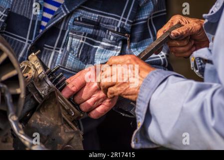 Zwei alte Männer, Automechaniker, die an rostigem Motor arbeiten, in einer Werkstatt. Reparaturservice Nahaufnahme zerknitterte schmutzige Hände blaue Kleidung Gear Truck DISAs Stockfoto