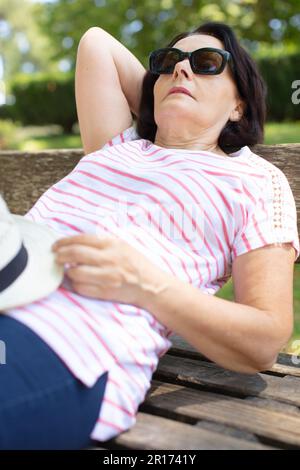 Die ältere Frau schläft auf der Bank im Sommerpark Stockfoto