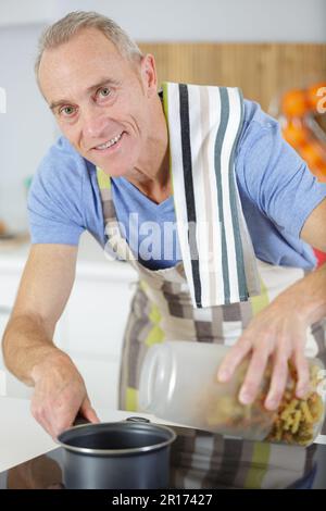 Ein älterer Mann mischt etwas in der Pfanne Stockfoto