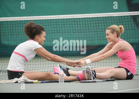 Frauen auf dem Tennisplatz beim Aufwärmen dehnen sich zusammen Stockfoto