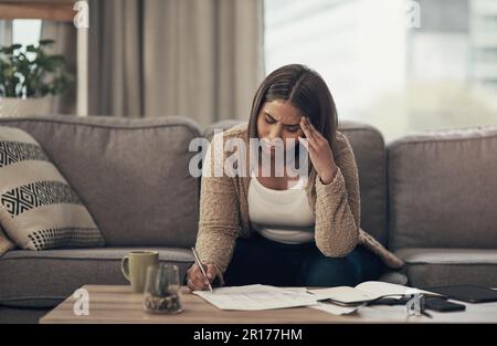 Es ist schwer, sich vom Netz der Schulden zu befreien. Eine junge Frau, die gestresst aussieht, als sie zu Hause Papierkram durchging. Stockfoto