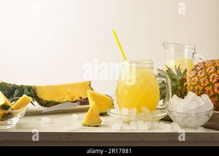 Ein Glas Ananasgetränk mit Eis auf dem Tisch mit zerstoßenem Eis und Obst und isoliertem Hintergrund. Vorderansicht. Horizontale Zusammensetzung. Stockfoto