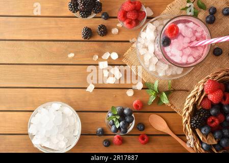 Kaltes Waldfruchtgetränk mit Beeren und zerstoßenem Eis auf einem Holztisch. Draufsicht. Horizontale Zusammensetzung. Stockfoto