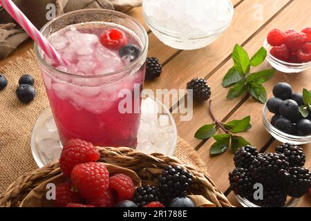 Fruchtgetränk mit Brombeeren, Himbeeren und Blaubeeren auf einem Holztisch mit Behältern voller Obst und Eis. Erhöhte Aussicht. Horizontale Kompositionierung Stockfoto