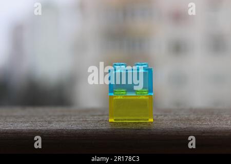 Bausteine eines Spielzeugbauers in den Farben der ukrainischen Flagge auf einem verblassten Holzgeländer über verschwommenen Wohnungen im Hintergrund Stockfoto
