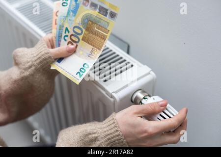 Eine Frau, die Geld vor dem Heizkörper hält. Bezahlung für Heizung im Winter Stockfoto