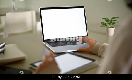 Nahaufnahme einer Frau, die ihren Laptop zur Verwaltung ihrer Arbeit zu Hause verwendet. Laptop-Computer-Modell mit weißem Bildschirm Stockfoto