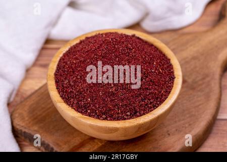 Sumac auf Holzhintergrund. Getrocknete gemahlene rote Sumac-Gewürze in einer Holzschüssel Stockfoto