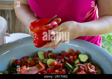 Eine Frau in ihren Händen schneidet bulgarischen Pfeffer über eine Schüssel Salat Stockfoto