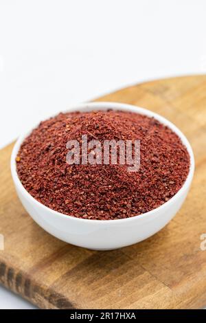 Sumac isoliert auf weißem Hintergrund. Getrocknete gemahlene rote Sumac-Gewürze in einer Holzschüssel Stockfoto