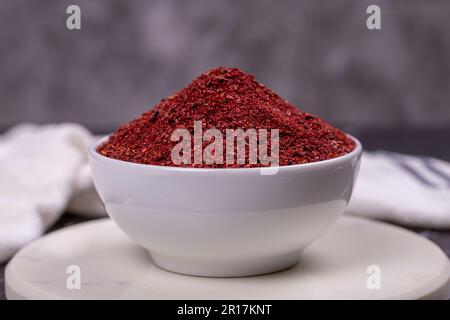 Sumac auf dunklem Hintergrund. Getrocknete gemahlene rote Sumac-Gewürze in einer Holzschüssel. Schließen Stockfoto