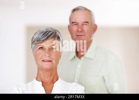 Selbstbewusste reife Frau mit Mann im Hintergrund. Porträt einer selbstbewussten, reifen Frau mit einem gutaussehenden Mann im Hintergrund. Stockfoto