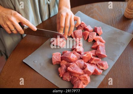 Frauenhände schneiden Rindfleischstücke auf einem Holztisch Stockfoto