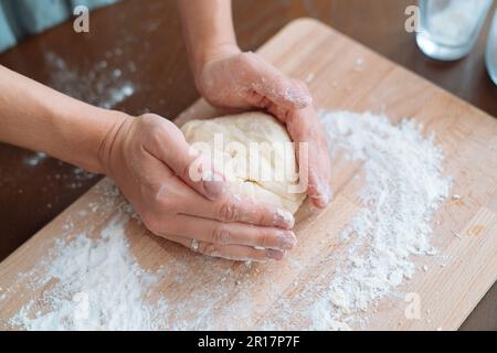 Frauenhände kneten Teig. Hände des Küchenchefs kneten Teig für Pizza. Kniescheibe Stockfoto