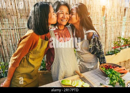 Fröhliche asiatische Mutter, die mit ihren Töchtern Spaß hat, während sie auf der Terrasse zuhause im Freien kocht - Familien- und Mutterschaftskonzept - Hauptfokus auf das Muttergesicht Stockfoto