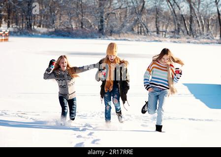 Drei Mädchen Rennen im Schnee auf einem gefrorenen See am Wintertag. Stockfoto