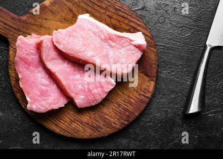 Rohe Schweinefleischscheiben und Messer auf rustikalem Schneidebrett aus der Nahaufnahme. Schweinelende Stücke. Stockfoto