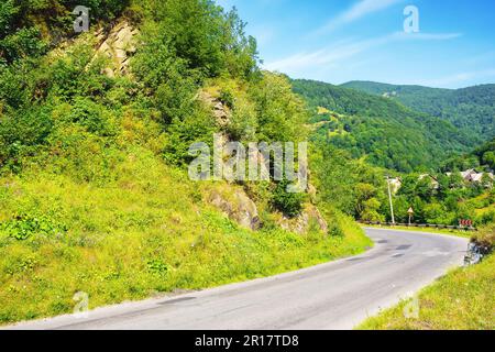 Die Straße führt durch die friedliche Landschaft und bietet Reisenden einen malerischen Pfad. Die ruhige Landschaft wird nur durch die majestätischen Berge auf t unterbrochen Stockfoto