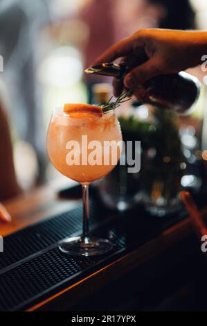 Nahaufnahme eines Barkeepers, der ein Getränk in ein Cocktailglas auf einem Bartisch gießt. Stockfoto
