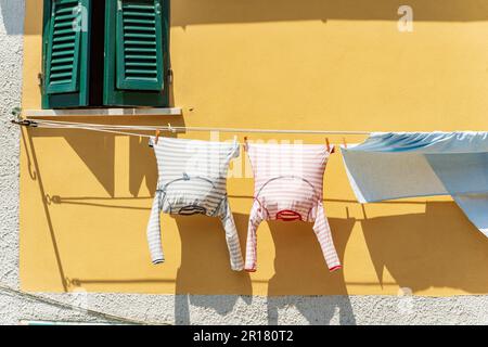 Wäsche hängt vor dem Fenster an einer Wäscheleine, um in der Sonne zu trocknen. Tellaro, Ligurien, Italien, Südeuropa. Zwei Pyjamas und ein Bettlaken. Stockfoto