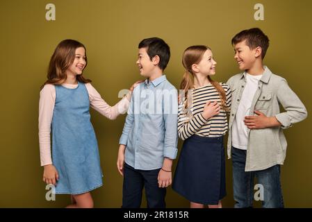 Lächelnde Kinder aus verschiedenen Rassen und Jugendliche in lässiger Kleidung, die miteinander sprechen, während sie den internationalen Tag des Kinderschutzes auf Khaki-Hintergrund feiern Stockfoto