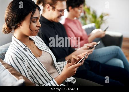 Technologie hilft, Wartezeiten zu vermeiden. Eine vielfältige Gruppe von Geschäftsleuten, die im Büro sitzen und auf ihren Handys SMS schreiben. Stockfoto