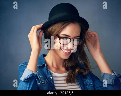 Tragen Sie Ihren Style ganz nach Ihren Wünschen. Eine seltsame junge Frau, die im Studio vor grauem Hintergrund lächelt. Stockfoto