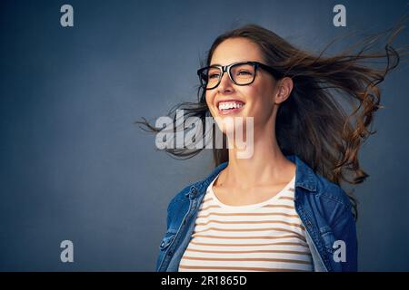 Mit einem Lächeln in die Zukunft blicken. Eine glückliche junge Frau, die im Studio Luft ins Gesicht geblasen hat. Stockfoto