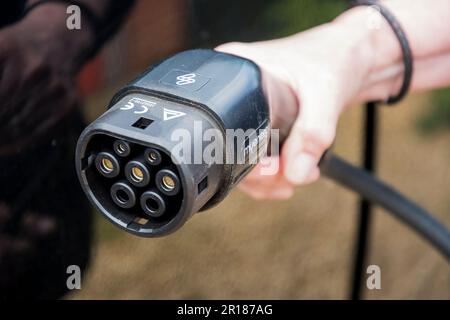 Eine Hand, die einen Stecker hält, um ein Elektrofahrzeug anzuschließen und zu laden. Stockfoto