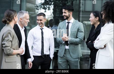 Gruppe von Geschäftsleuten, die ein zwangloses Meeting im Freien veranstaltet. Bürokollegen, die auf der Straße stehen und reden und lächeln. Stockfoto