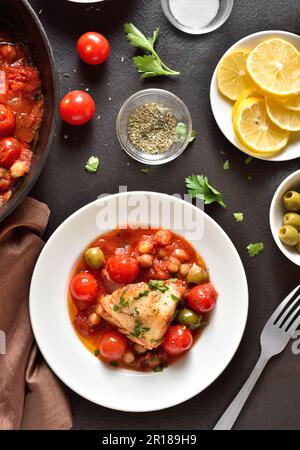 Kabeljaueintopf mit Kichererbsen, Kirschtomaten und Oliven auf dem Teller auf dunklem Steingrund. Draufsicht, flach liegend Stockfoto