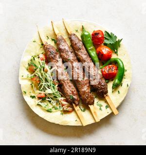 Kebabs mit frischem Gemüse auf Fladenbrot auf hellem Steinhintergrund. Nahaufnahme Stockfoto