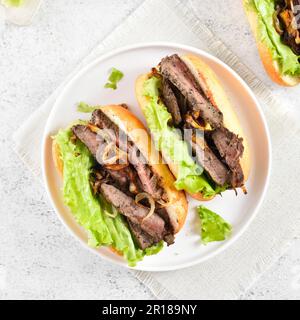 Rindfleisch-Sandwiches mit karamellisierten Zwiebeln auf dem Teller auf hellem Steingrund. Draufsicht, flach liegend Stockfoto