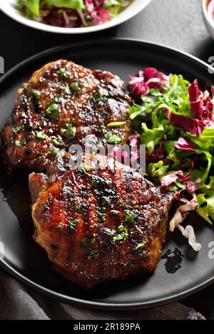 Nahaufnahme von gebratenem Schweinesteak mit Salat aus frischem Gemüse auf schwarzem Stein Hintergrund. Stockfoto