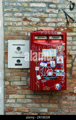 Aufkleber bedeckte rote Mailbox neben einer alten Sprechanlage an einer Ziegelwand, Venedig, Venetien, Italien Stockfoto