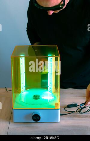 Mann mit Brille, der vor Gebrauch eine Wasch- und Heilungsmaschine mit UV-Licht justiert, für 3D-Harzdrucker Stockfoto