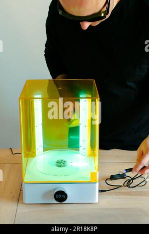 Mann mit Brille, der vor Gebrauch eine Wasch- und Heilungsmaschine mit UV-Licht justiert, für 3D-Harzdrucker Stockfoto