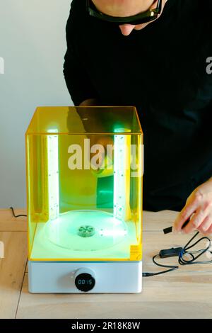 Mann mit Brille, der vor Gebrauch eine Wasch- und Heilungsmaschine mit UV-Licht justiert, für 3D-Harzdrucker Stockfoto