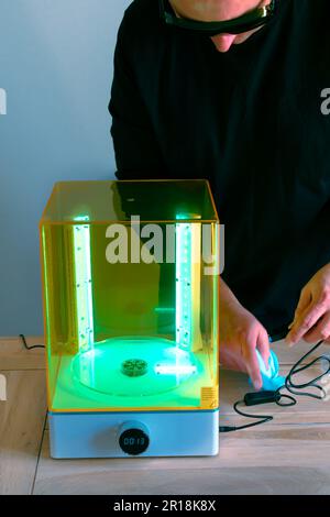 Mann mit Brille, der vor Gebrauch eine Wasch- und Heilungsmaschine mit UV-Licht justiert, für 3D-Harzdrucker Stockfoto