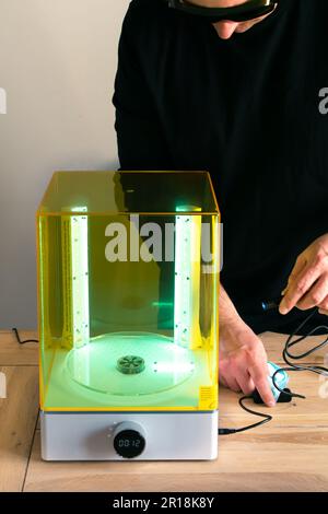 Mann mit Brille, der vor Gebrauch eine Wasch- und Heilungsmaschine mit UV-Licht justiert, für 3D-Harzdrucker Stockfoto