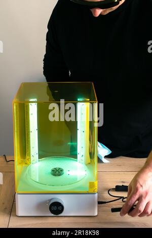 Mann mit Brille, der vor Gebrauch eine Wasch- und Heilungsmaschine mit UV-Licht justiert, für 3D-Harzdrucker Stockfoto